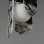 Close view of black-veined white marble panels and a frosted glass globe on this Clérachic pendant, on a grey backdrop.