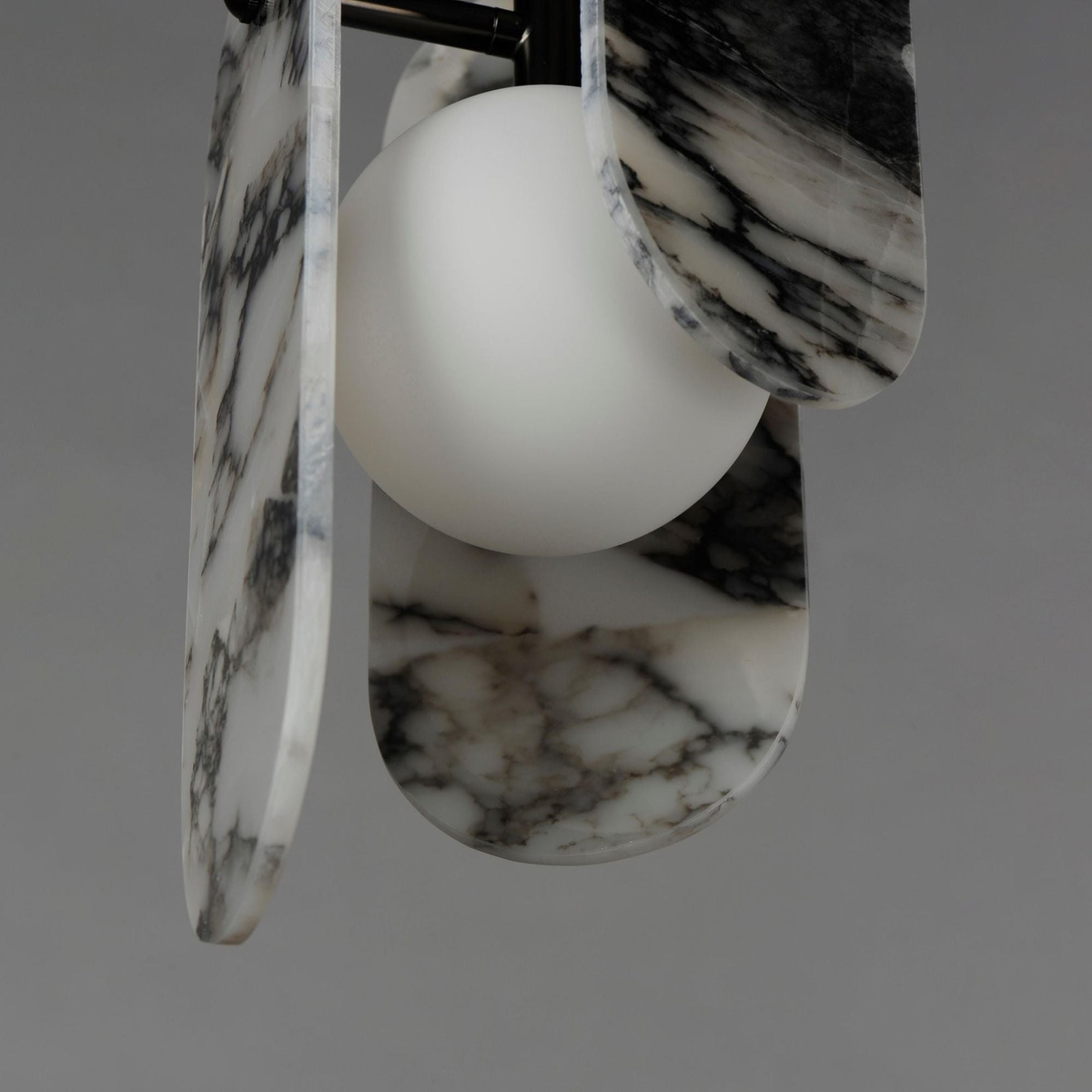 Close view of black-veined white marble panels and a frosted glass globe on this Clérachic pendant, on a grey backdrop.