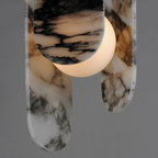 Close view of warm light glowing through the black-veined marble panels on this Clérachic pendant, against a grey backdrop.