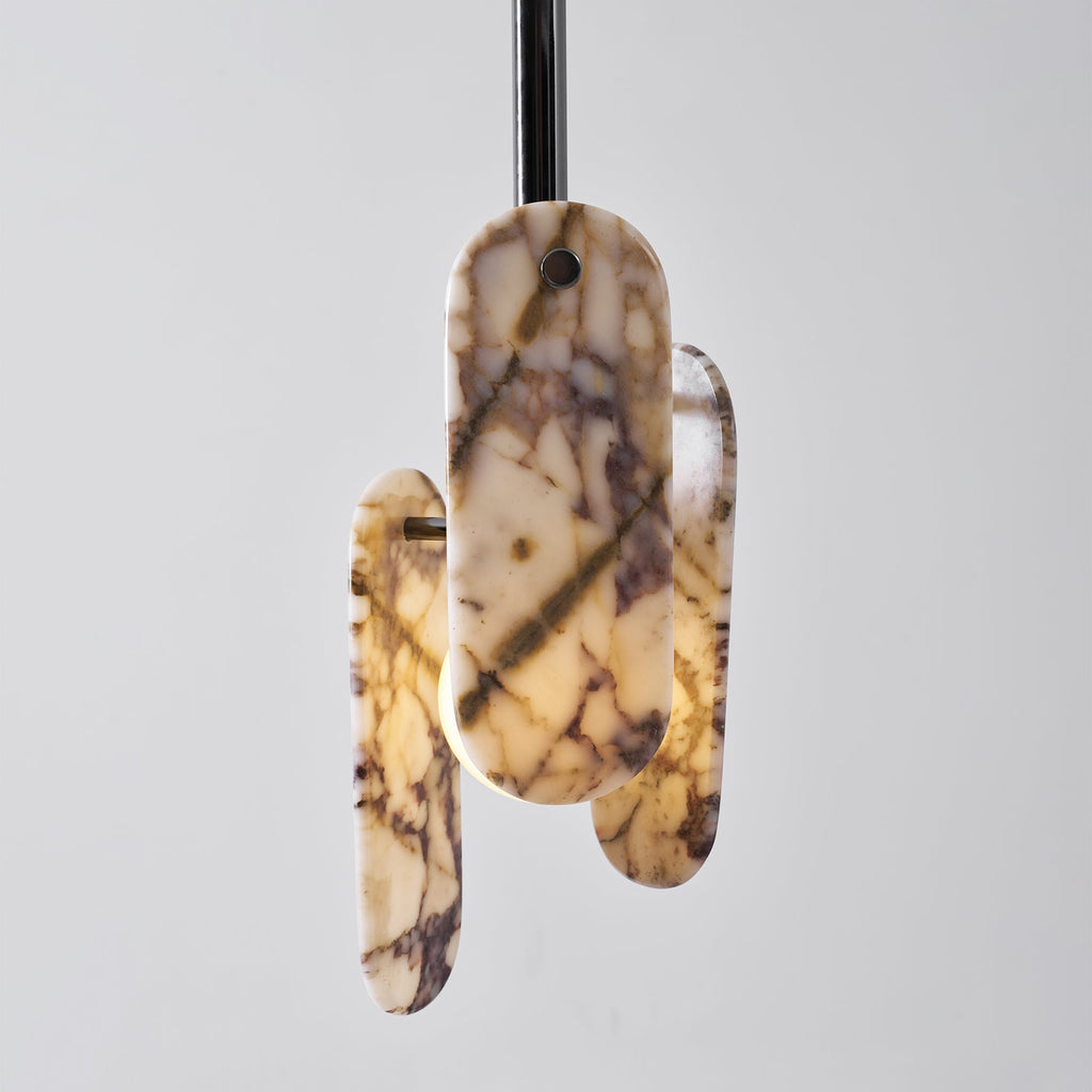 This Clérachic pendant in a cream marble version, lit warm, with a frosted globe showing between the oval stone panels.