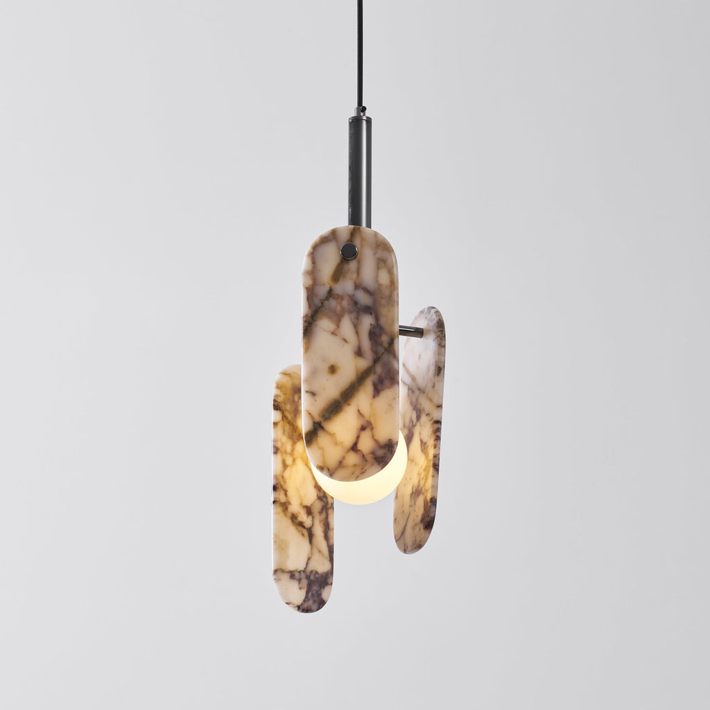 A cream marble Clérachic pendant glowing amber through its oval panels, on a black stem against a pale grey backdrop.