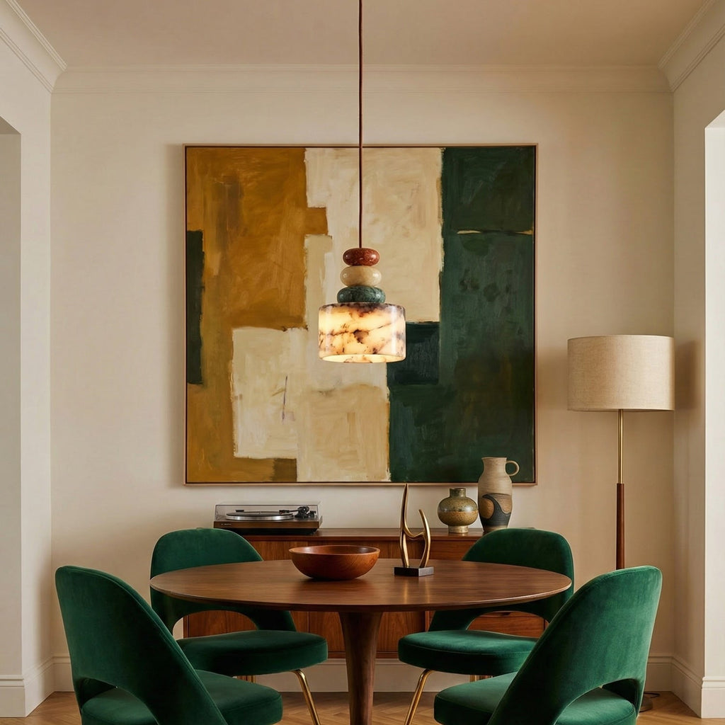 Small Clérachic pendant hung over a round walnut dining table with green velvet chairs, in front of a large abstract painting.