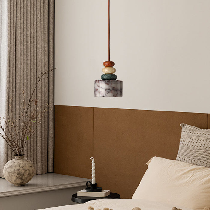 Above a bed with cream pillows, a Clérachic pendant hangs against a white wall, with a stone vase of branches and a candle nearby.