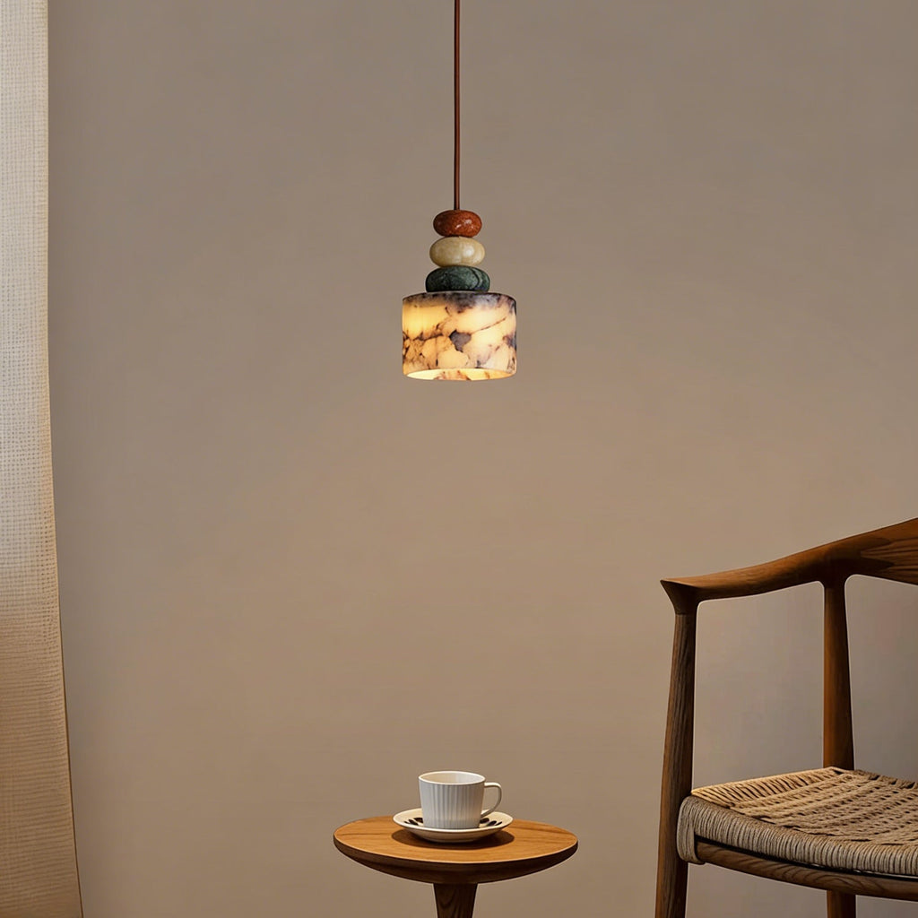 Distant view of a lit Clérachic pendant on a taupe wall, with a wooden armchair and a small round table with a cup beside it.