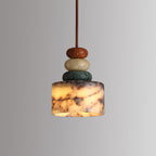 Lit Clérachic pendant on a grey backdrop, the marble drum glowing warm from within while the beads above stay rust, cream and green.