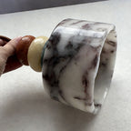 Held in one hand on a pale surface, the marble drum shade of this Clérachic pendant shows thick walls and dark veining.