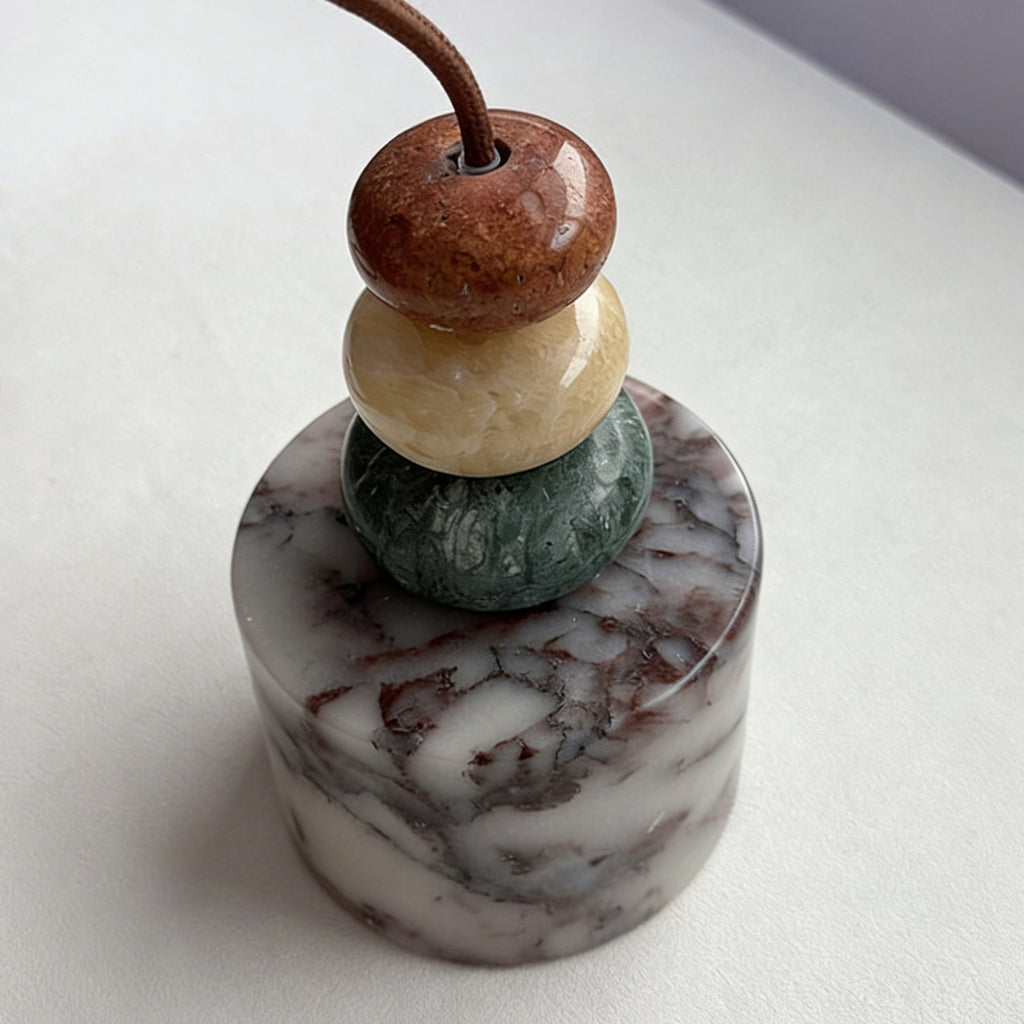Close view of the three stone beads and the marble drum on this Clérachic pendant, resting on a pale surface with the cord curling away.