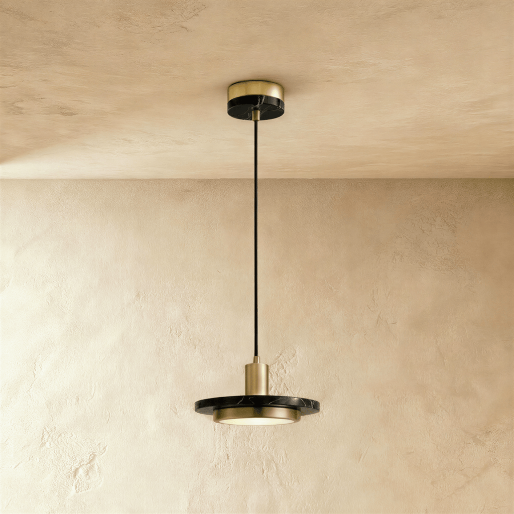 Clérachic brass-finish pendant light with a black marble plate and a glowing round diffuser on a limewash wall.