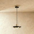 Clérachic brass-finish pendant light with a black marble plate and a glowing round diffuser on a limewash wall.