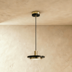 Clérachic brass-finish pendant light with a black marble plate and a glowing round diffuser on a limewash wall.