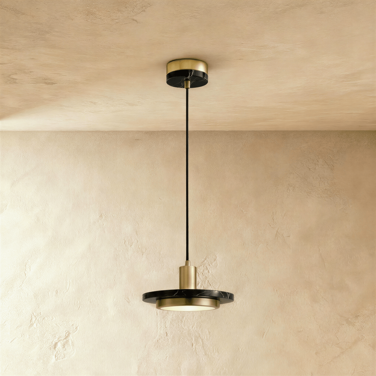 Clérachic brass-finish pendant light with a black marble plate and a glowing round diffuser on a limewash wall.
