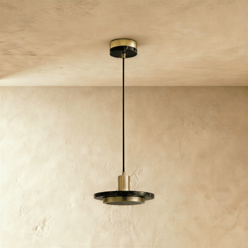 Clérachic brass-finish pendant with a black marble plate and a switched-off round diffuser, on a limewash wall.