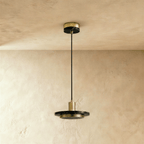Clérachic brass-finish pendant with a black marble plate and a switched-off round diffuser, on a limewash wall.
