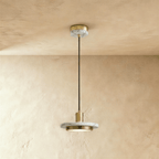 Clérachic brass-finish pendant light with a white veined marble plate and round diffuser on a limewash wall.
