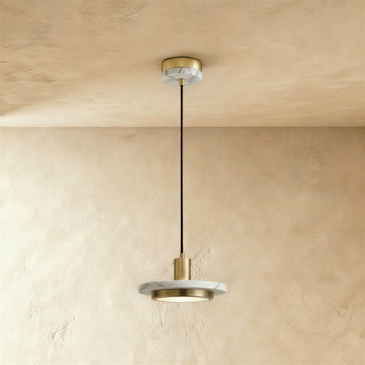 Clérachic brass-finish pendant light with a white veined marble plate and round diffuser on a limewash wall.