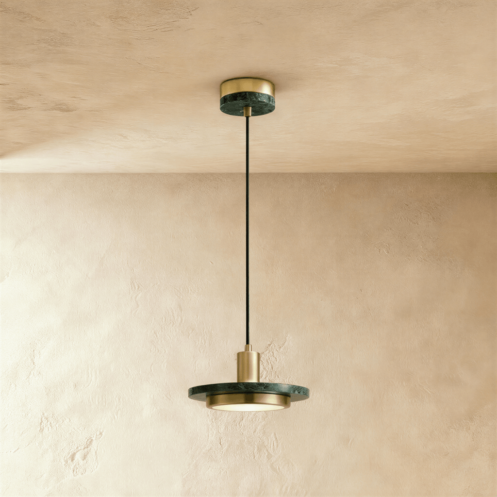 Clérachic brass-finish pendant light with a dark green marble plate and a round diffuser on a limewash wall.
