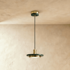 Clérachic brass-finish pendant light with a dark green marble plate and a round diffuser on a limewash wall.