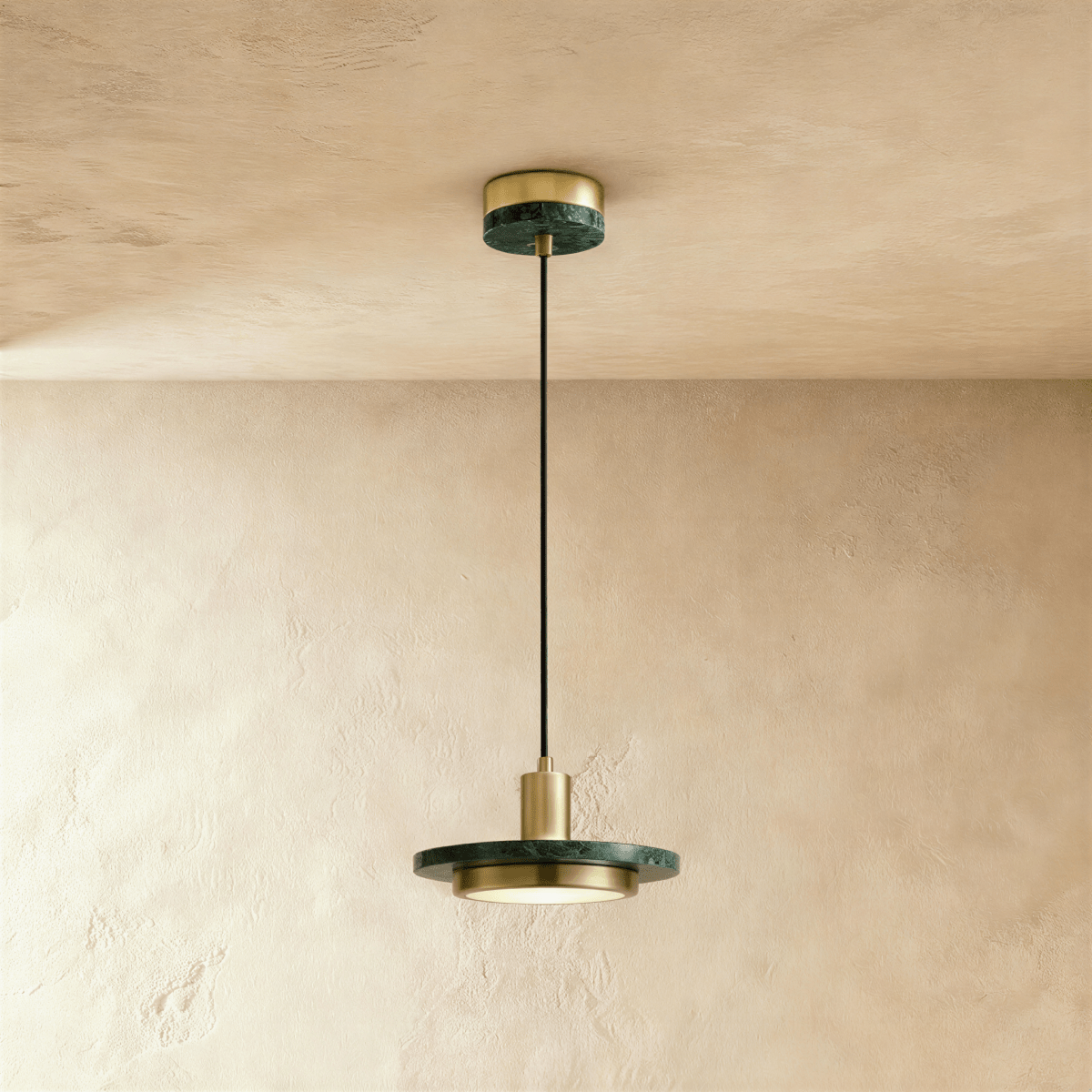 Clérachic brass-finish pendant light with a dark green marble plate and a round diffuser on a limewash wall.
