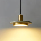 Close view of the Clérachic pendant light, a brass cylinder and white marble plate above a softly glowing round diffuser.