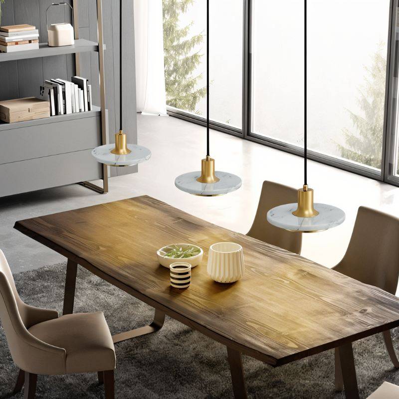Clérachic row of three white marble and brass pendant lights hung low over a rustic wooden dining table.