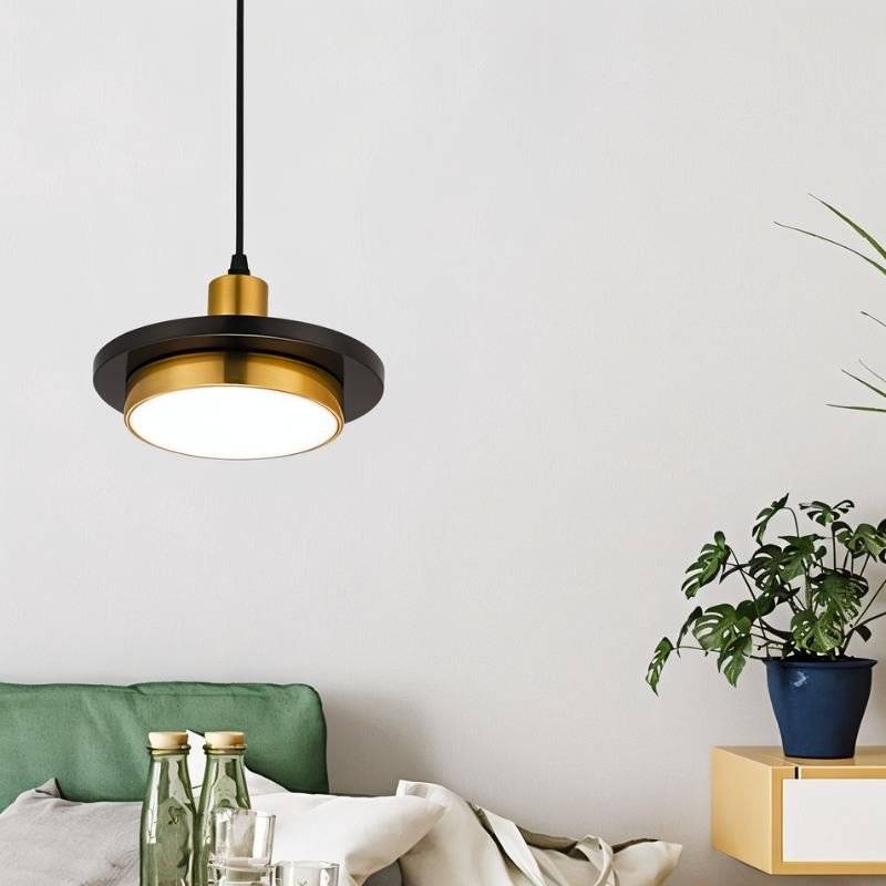 Clérachic black marble and brass pendant light with a lit white diffuser hanging beside a green cushion and plant.