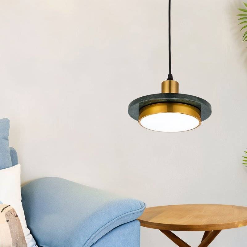 Clérachic dark green marble and brass pendant light with a lit diffuser beside a light blue sofa and wooden side table.