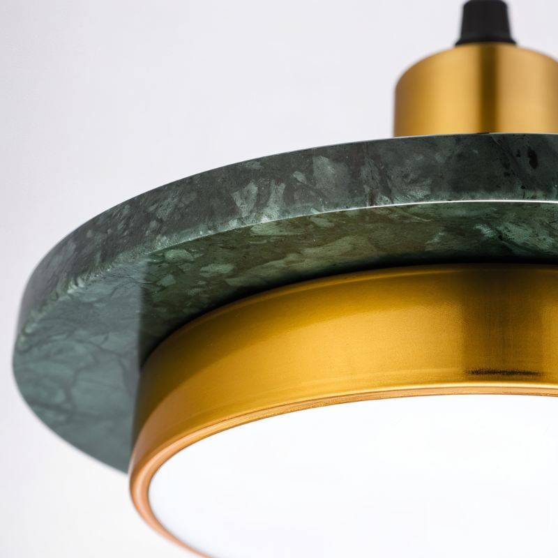 Macro of the Clérachic pendant light showing the veined dark green marble plate, brass ring and white diffuser.