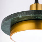 Macro of the Clérachic pendant light showing the veined dark green marble plate, brass ring and white diffuser.