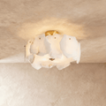 Clérachic semi-flush ceiling light with veined white stone slabs glowing warmly, brass canopy above, on a plaster ceiling.