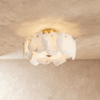 Clérachic semi-flush ceiling light with veined white stone slabs glowing warmly, brass canopy above, on a plaster ceiling.
