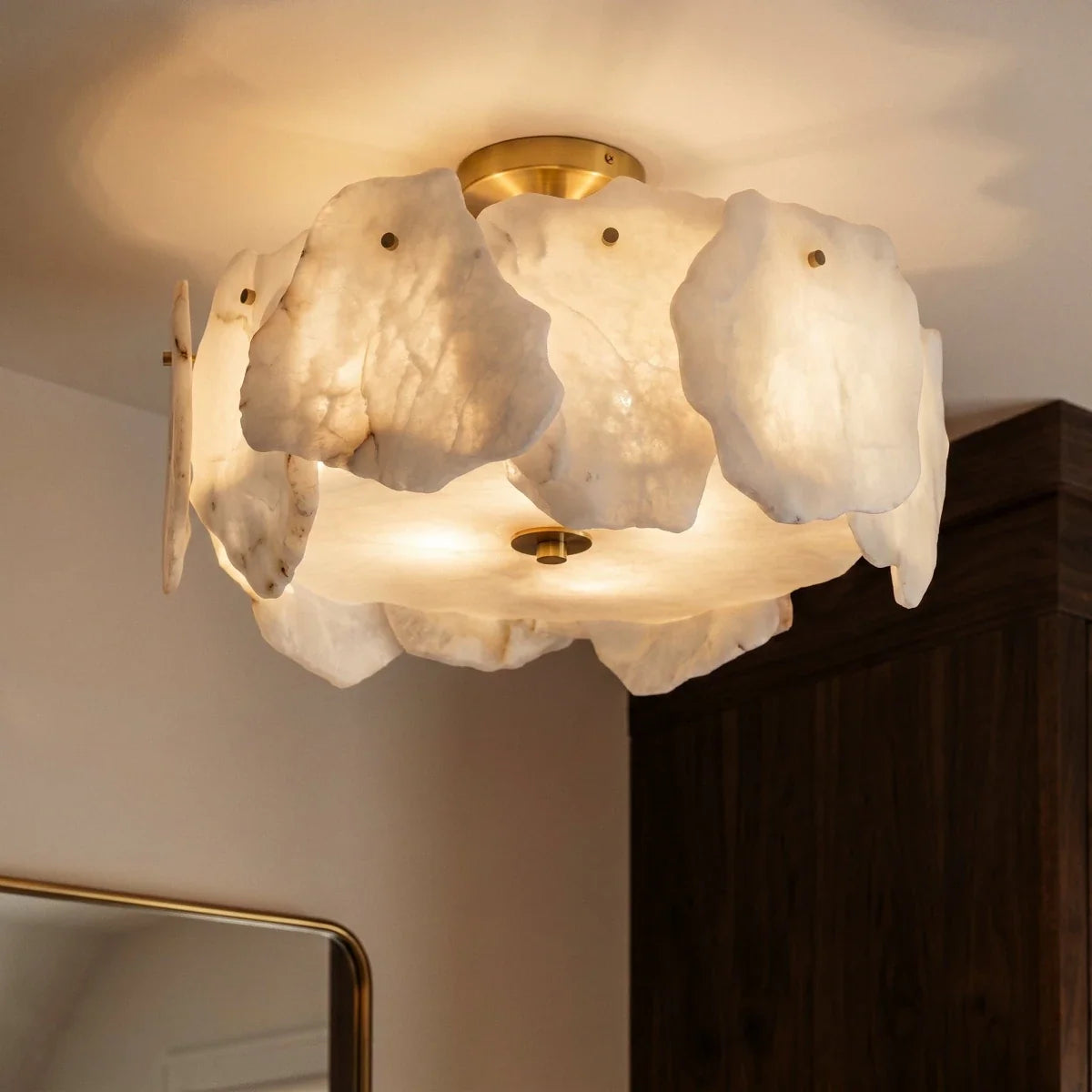 Close view of a Clérachic ceiling light, natural white stone slabs lit from within, held by small brass studs on a brass canopy.