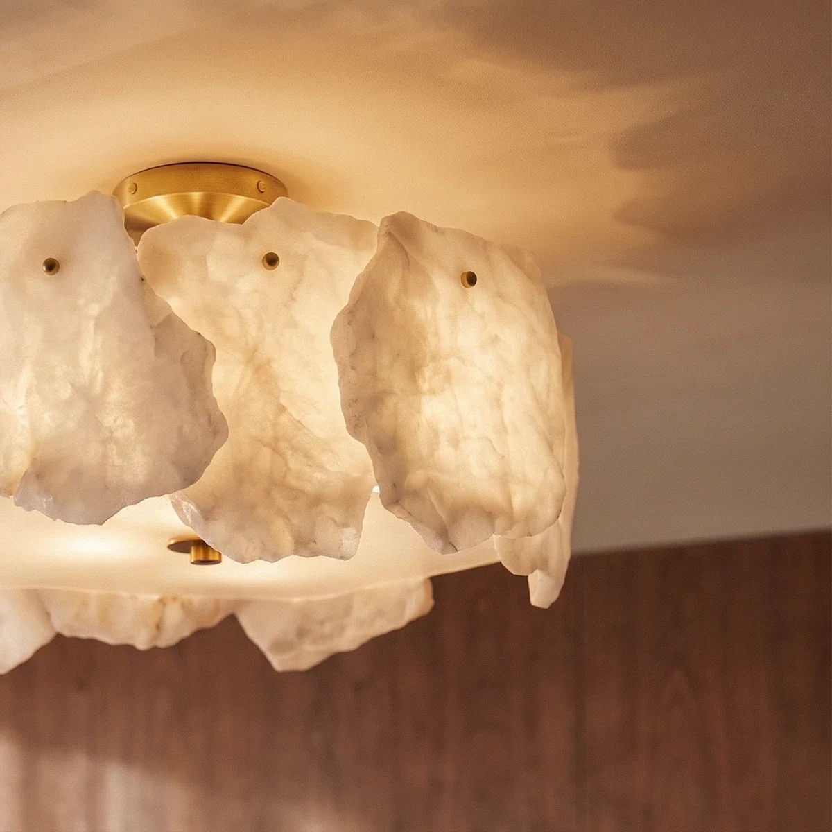 Close view of a Clérachic ceiling light, translucent veined alabaster slabs with brass studs glowing against a walnut-panelled wall.