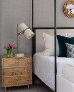 Bedside scene with a small Clérachic table lamp on a burl-wood nightstand, its tilted white shade beside a canopy bed and teal cushions.