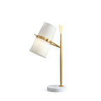 Gold-stemmed Clérachic table lamp with a white marble base, its white shade tipped to the left, on a white background.