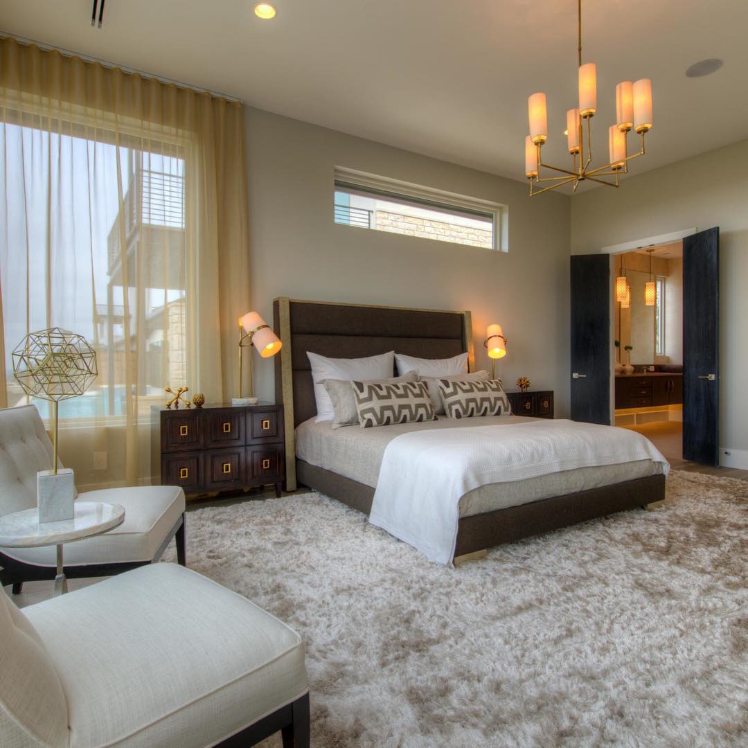 Bedroom scene with a Clérachic table lamp among the furnishings, with a tufted bed, a shag rug and a candle-style chandelier overhead.