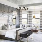 Large bedroom with a Clérachic table lamp on a bedside table, a tufted grey bed, a black multi-arm chandelier and a bay window.