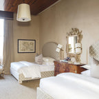 Twin-bed room with a Clérachic table lamp beside the headboards, a carved gilt mirror and a drum pendant hanging above.