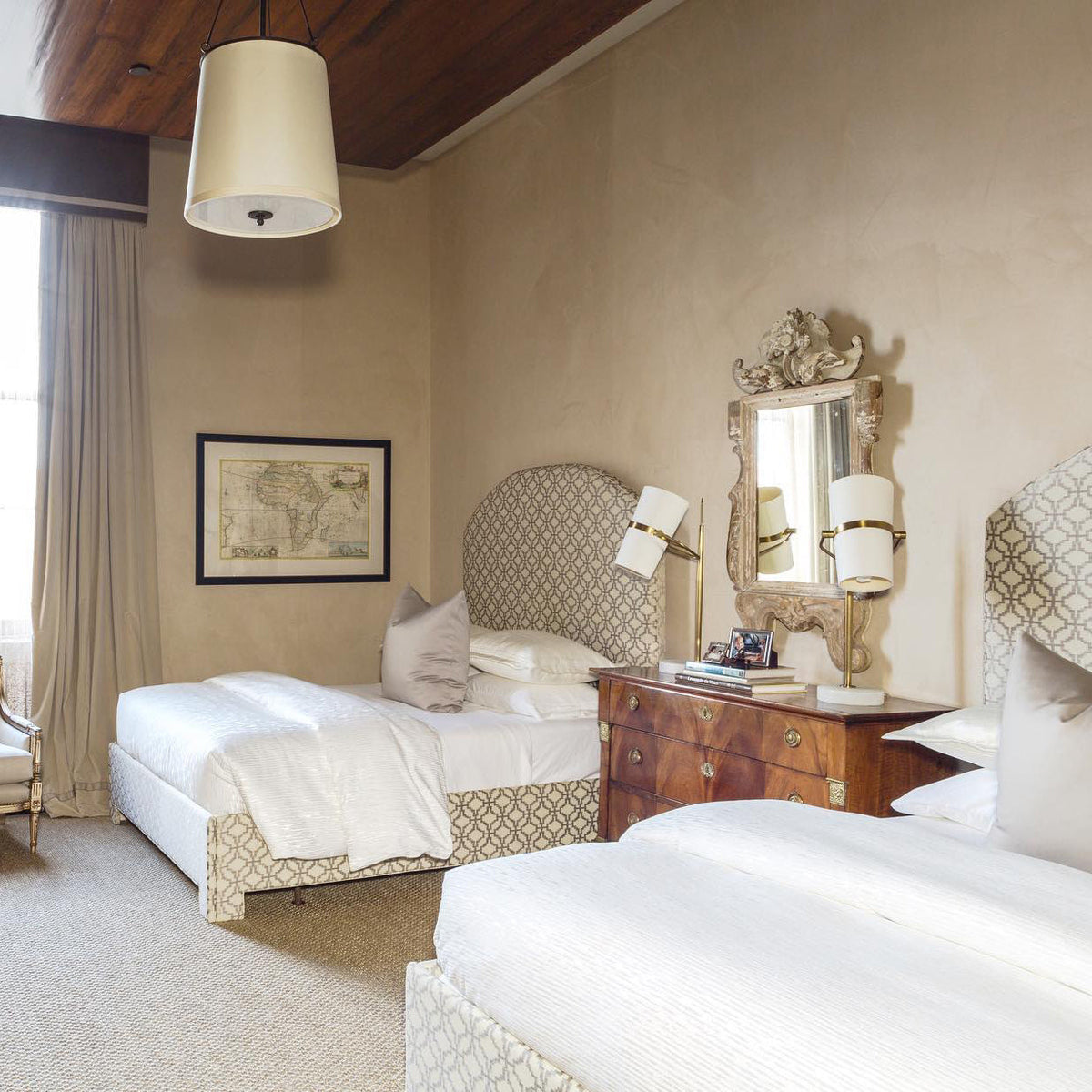 Twin-bed room with a Clérachic table lamp beside the headboards, a carved gilt mirror and a drum pendant hanging above.