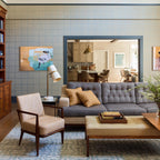 Beside a blue-framed doorway, a Clérachic table lamp sits lit on a side table behind a grey tufted sofa and an apricot armchair.