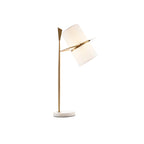 Clérachic table lamp with a gold stem and white marble base, its white shade angled up and to the right, on a plain white background.