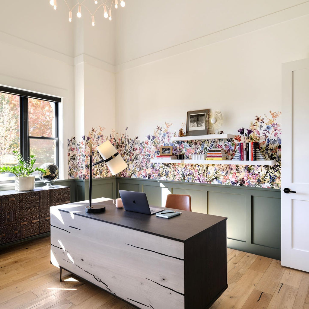 Home office with a Clérachic table lamp on a dark desk with a laptop, a floral wallpaper band, green panelling and open shelves.