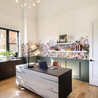 Home office with a Clérachic table lamp on a dark desk with a laptop, a floral wallpaper band, green panelling and open shelves.