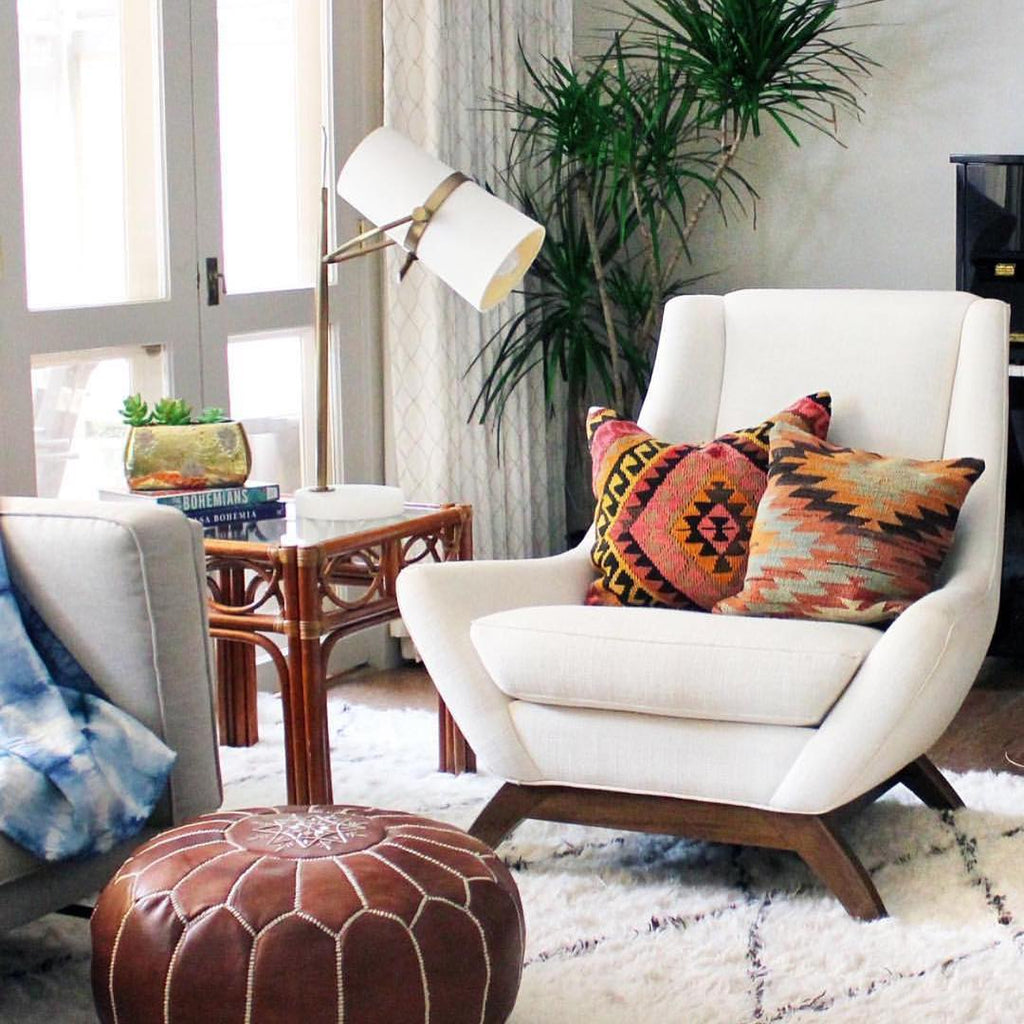 Reading corner with a Clérachic table lamp on a rattan side table beside a cream armchair, kilim cushions and a tan leather pouf.