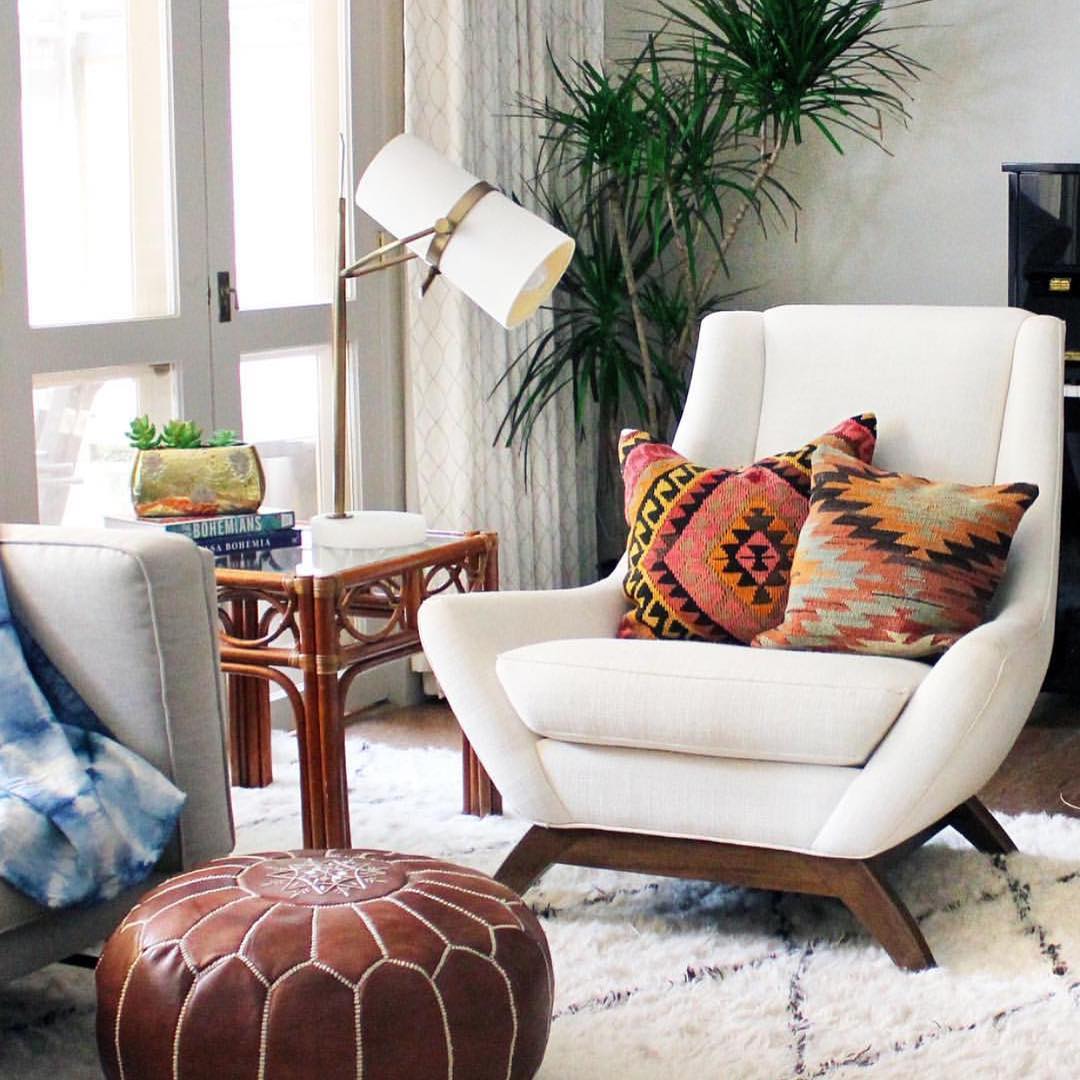 Reading corner with a Clérachic table lamp on a rattan side table beside a cream armchair, kilim cushions and a tan leather pouf.