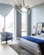 Blue-grey bedroom with a Clérachic table lamp on the bedside table, a bed with a navy throw, an armchair and a gold branching chandelier above.