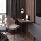 Slim wall-hung desk with a laptop and a lit Clérachic table lamp, beside a taupe chair and dark ribbed curtains.