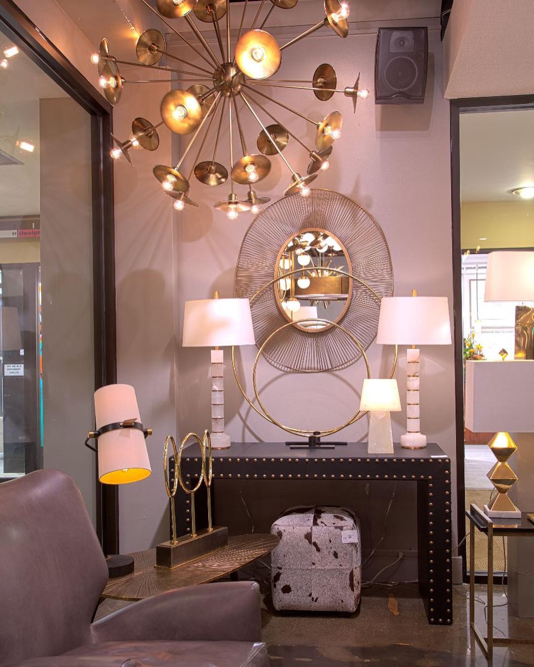 Console table with a Clérachic table lamp, its shade glowing orange-pink, between two white lamps under a gold starburst chandelier.