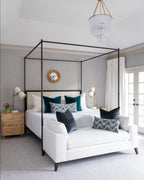 Canopy-bed bedroom with Clérachic table lamps on the burl-wood bedside chests, a white sofa at the foot and a beaded chandelier above.