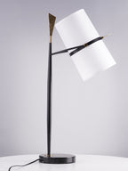 Black-stemmed Clérachic table lamp with a black marble base on a white round table, the white shade tilted right against a grey backdrop.