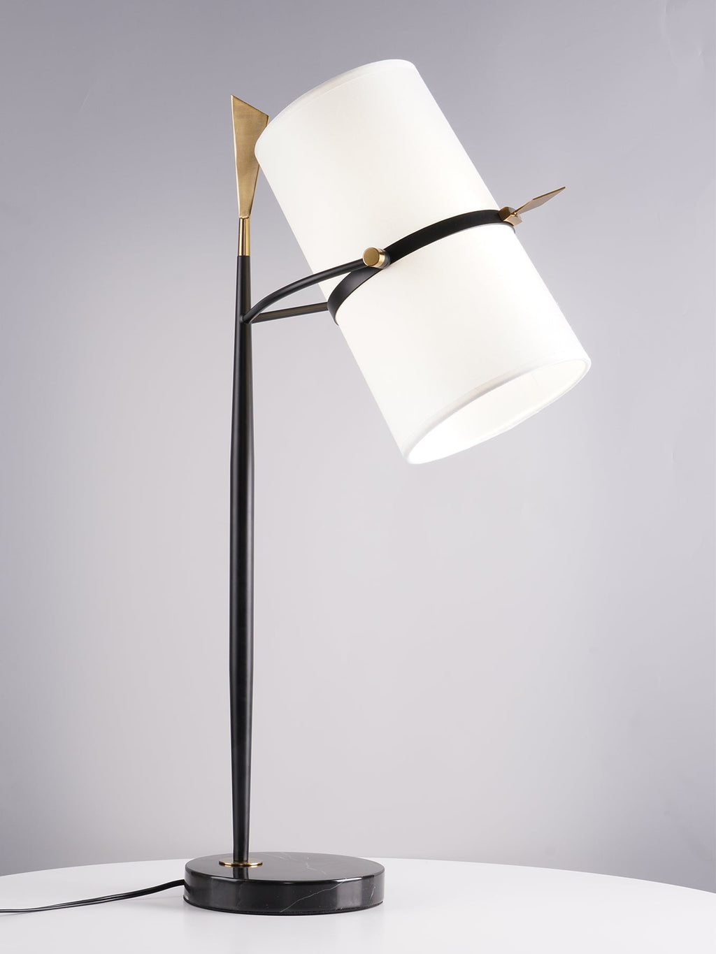 Three-quarter view of this Clérachic table lamp, shade angled sharply right, on a black stem and black marble base with a cord on a white table.